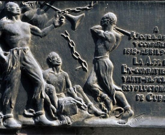 bronze bas-relief monument to Jose Aponte; the image is of an Afro-Cuban man striking the chains off two other enslaved men