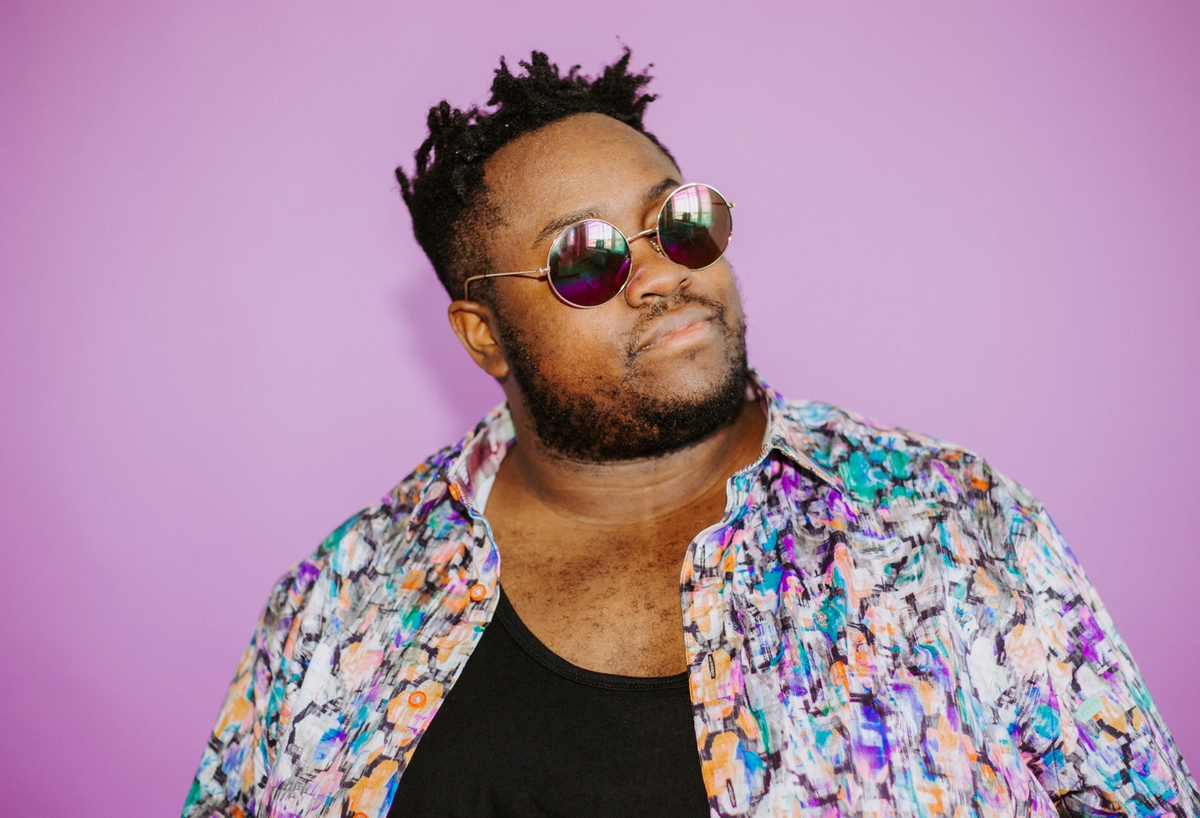 Image of black man with sunglasses, colorful button up on purple background