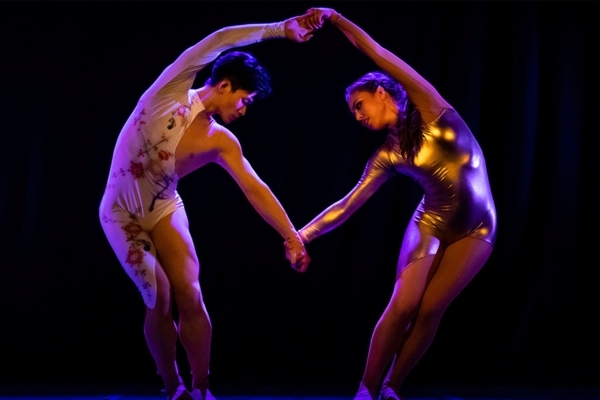 Two dancers bent towards each other holding hands
