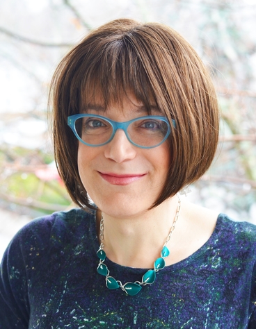 Photo of a woman with short brown hair, blue glasses, smiling