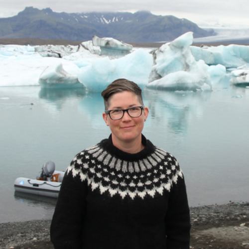 Woman with short cropped hair in sweater standing in front of Icelandic glacier